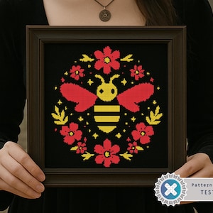 May include: Framed cross-stitch art featuring a stylized bee with red wings and yellow body, surrounded by red flowers and yellow leaves on a black background. The artwork is in a brown frame.