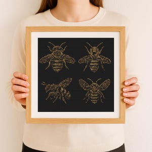 Op de afbeelding: Een ingelijst drukwerk met vier gouden bijen op een zwarte achtergrond. De bijen zijn gedetailleerd en ingewikkeld, in vintage stijl.