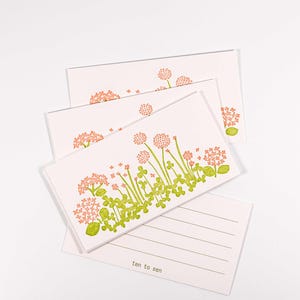 May include: A stack of light pink notecards with a floral design in green and peach. The cards feature a row of stylized flowers and the text "ten to see" at the bottom. The cards are blank inside.