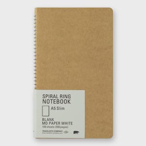 May include: A5 Slim spiral ring notebook with a kraft paper cover. The notebook has a white label with the text "SPIRAL RING NOTEBOOK", "BLANK MD PAPER WHITE", and "100 sheets (200 pages)". The notebook is made by Traveler's Company.