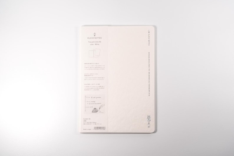 K&ouml;nnte beinhalten: Ein cremefarbenes Notizbuch mit dem Text "ALBUM NOTES" und japanischem Text. Das Notizbuch hat ein Rastermuster und ist offen, um leere Seiten zu zeigen. Die R&uuml;ckseite des Notizbuchs hat gedruckten Text und einen Barcode.