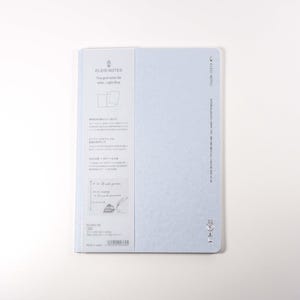 K&ouml;nnte beinhalten: Ein hellblaues Notizbuch mit dem Text "BLEU NOTES" und anderem Text auf Japanisch. Das Notizbuch hat ein Rastermuster und liegt auf einer wei&szlig;en Oberfl&auml;che.