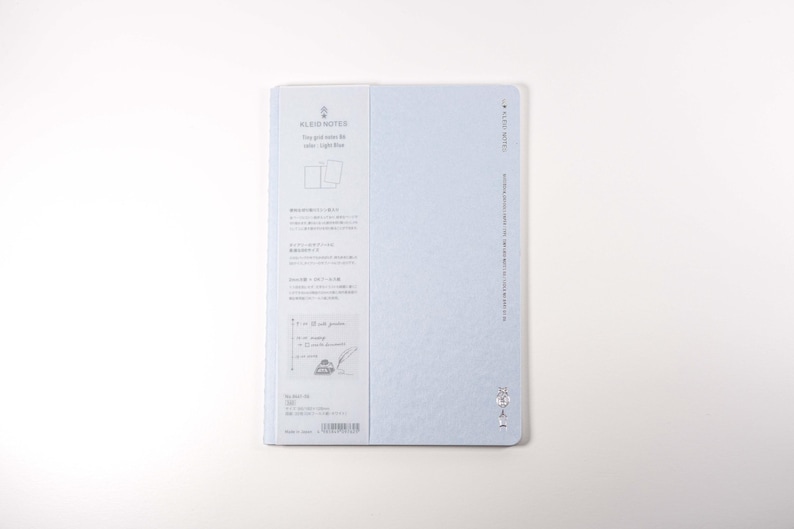 K&ouml;nnte beinhalten: Ein hellblaues Notizbuch mit dem Text "BLEU NOTES" und anderem Text auf Japanisch. Das Notizbuch hat ein Rastermuster und liegt auf einer wei&szlig;en Oberfl&auml;che.