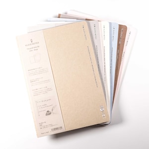 Puede incluir: Una pila de cuadernos con cubiertas de varios colores, incluyendo beige, blanco y azul. Los cuadernos tienen un diseño sencillo y el texto "KLEID NOTES" es visible en la cubierta. Los cuadernos están abanicados, mostrando los diferentes colores.