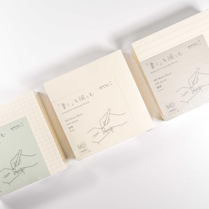 May include: Three different MD Paper notebooks with grid, lined, and blank pages. Each notebook has a cream-colored cover with the text "書く"を愉しむ" and a drawing of a hand writing with a pen.