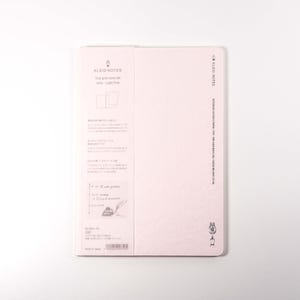 K&ouml;nnte beinhalten: Ein hellrosa Notizbuch mit dem Text "KLEID NOTES" und japanischem Text. Das Notizbuch hat einen weichen Einband und ein schlichtes Design. Das Notizbuch befindet sich auf wei&szlig;em Hintergrund.