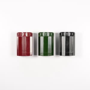 Puede incluir: Tres sacapuntas vintage en rojo, verde y negro. Cada sacapuntas tiene una forma hexagonal y un diseño acanalado.
