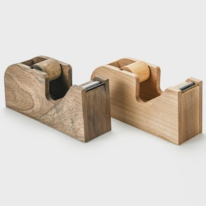 May include: Two wooden tape dispensers. One is a darker brown with visible wood grain, and the other is a lighter, natural wood color. Both have a similar design with a roller for the tape.