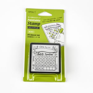 May include: A green and white package for a paint-based stamp. The stamp is black and white and features a calendar with the text "habit tracker" and "Let's try it!" The stamp is oil-based ink.