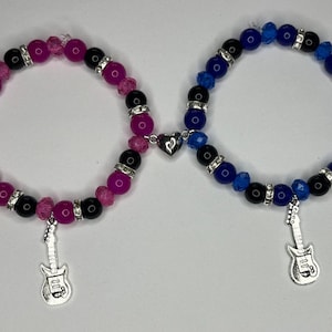 May include: Two beaded bracelets. One is pink and black with a star and guitar charm. The other is blue and black with a star and guitar charm. Both bracelets have a heart-shaped magnetic clasp.