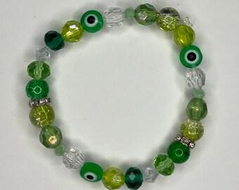 May include: Green and clear glass bead bracelet with evil eye charms. The bracelet has a silver accent on the beads.
