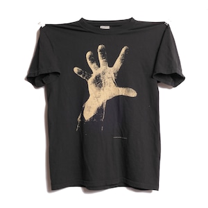 May include: A black t-shirt featuring a tan hand graphic. The graphic is a stylized open hand with the fingers spread. The t-shirt is hanging against a white background.