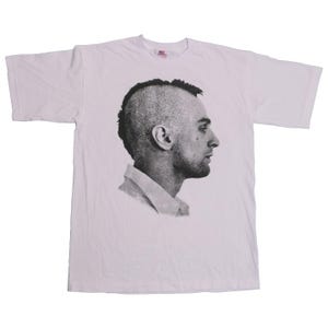 Puede incluir: Camiseta blanca con una imagen en blanco y negro de un hombre con un peinado mohicano.