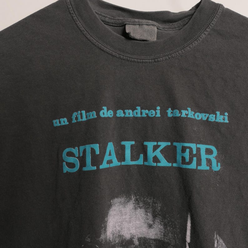 May include: A black t-shirt with a teal blue graphic print of the text "un film de andrei tarkovski" and "STALKER".