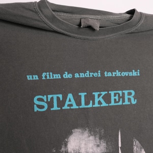 May include: A dark gray t-shirt with a blue graphic print of the text "un film de andrei tarkovski" and "STALKER".