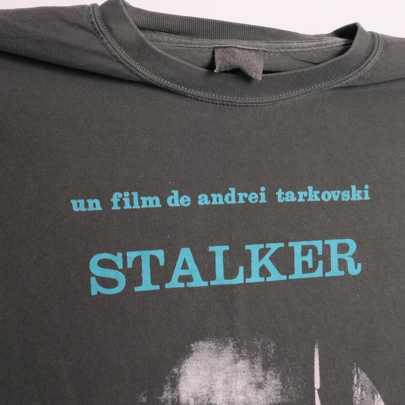 May include: A dark gray t-shirt with a blue graphic print of the text "un film de andrei tarkovski" and "STALKER".