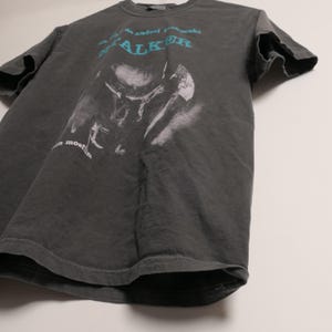 May include: A dark gray t-shirt with a faded image of a person wearing a hat and the text "Andrei Tarkovsky Stalker a most film".
