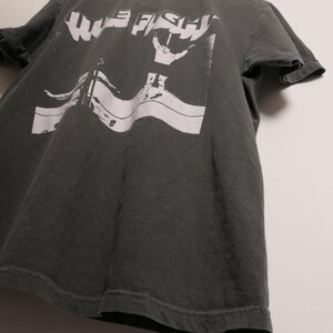 May include: A dark gray t-shirt with a white graphic print of the words "WIFE FISH" and a hand making a peace sign.
