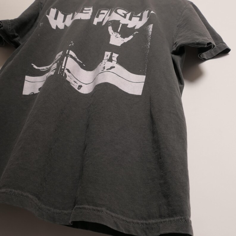 May include: A dark gray t-shirt with a white graphic print of the words "WIFE FISH" and a hand making a peace sign.