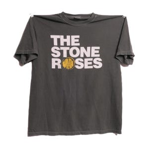 Op de afbeelding: Een donkergrijs T-shirt met de bandnaam "The Stone Roses" gedrukt in witte letters met een gele citroen afbeelding.