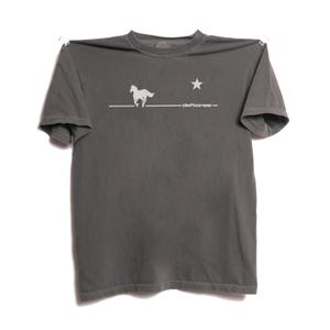 Könnte beinhalten: Graues T-Shirt mit einem weißen Aufdruck eines galoppierenden Pferdes, eines Sterns und dem Bandnamen "deftones". Das Shirt besteht aus einem weichen Material und hat kurze Ärmel. Das Design ist mittig auf der Vorderseite des Shirts platziert.