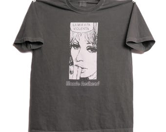 May include: A dark gray t-shirt with a black and white illustration of a woman's face and the text "La mia vita violenta" in a speech bubble above her head. The text "Blonde Redhead" is printed below the illustration.