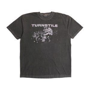 May include: Dark gray t-shirt with the word "TURNSTILE" in white block letters across the top. Below the text is a black and white graphic of a crowd of people. The shirt has short sleeves and a crew neck.