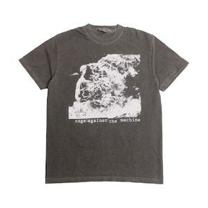May include: Dark gray t-shirt featuring a black and white graphic of a person in flames. The text "rage against the machine" is printed in white below the graphic. The shirt has short sleeves and a crew neck.