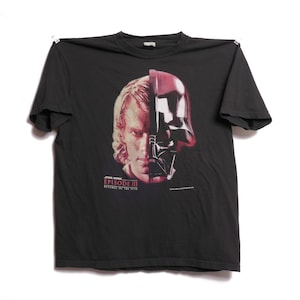 Könnte beinhalten: Schwarzes T-Shirt mit einem geteilten Bild von Anakin Skywalker und Darth Vader. Die Grafik ist in Rot-, Schwarz- und Weißtönen gehalten. Der Text "STAR WARS EPISODE III REVENGE OF THE SITH" ist darunter gedruckt.
