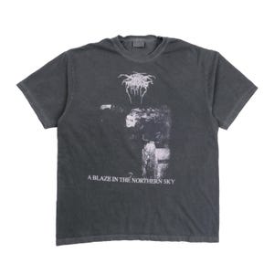 Op de afbeelding: Donkergrijs t-shirt met een zwart-witte afbeelding. De afbeelding bevat een gestileerde afbeelding en de tekst "A BLAZE IN THE NORTHERN SKY". Het shirt heeft een ronde hals en korte mouwen.