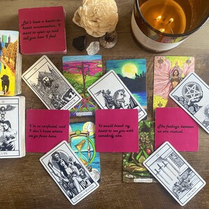 May include: A spread of tarot cards on a wooden table. The cards are arranged in a circle with a few cards overlapping. The cards are all different colors and have different images on them. The cards are surrounded by a variety of objects, including a candle, a crystal, and a wooden flower.