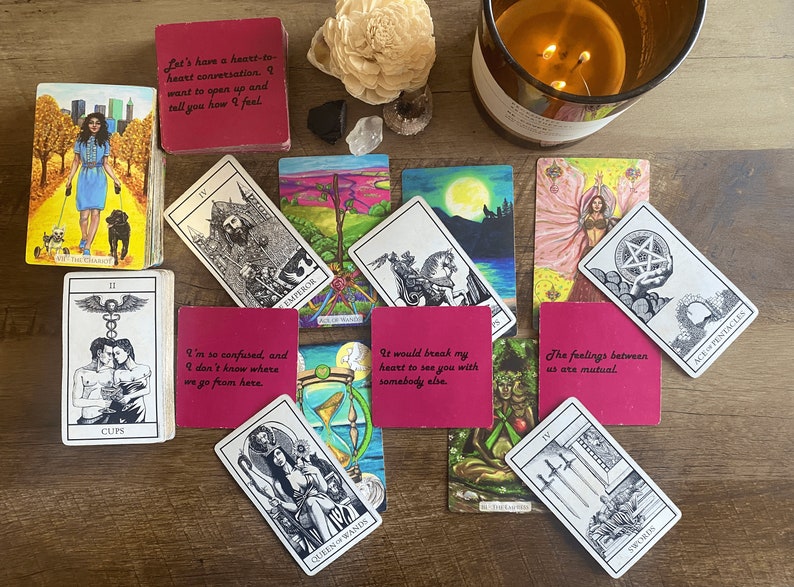 May include: A spread of tarot cards on a wooden table. The cards are arranged in a circle with a few cards overlapping. The cards are all different colors and have different images on them. The cards are surrounded by a variety of objects, including a candle, a crystal, and a wooden flower.