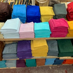 May include: A shelf display of various colors of leather, stacked in rows. The leather is in shades of brown, blue, green, yellow, pink, red, and gray.