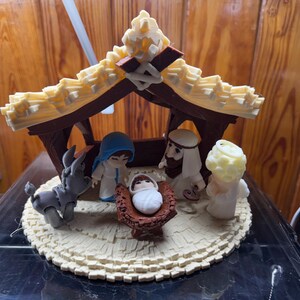 May include: A nativity scene figurine set with a brown wooden stable, a white and brown donkey, a blue robed Mary, a white robed Joseph, a baby Jesus in a brown manger, and a white angel.