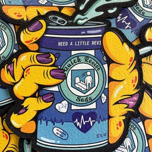 May include: A sticker featuring a blue soda can design with the text "Quick Revive Soda" and "Need a Little Revive". The can has a heart rate graphic and reads "12 FL OZ" and "115 Calories Per Dose". The sticker is held by yellow hands with purple nails.