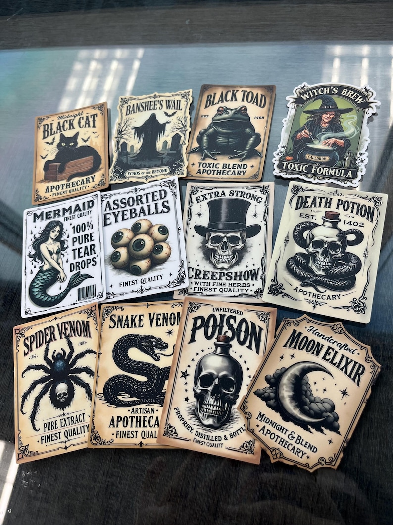 K&ouml;nnte beinhalten: Eine Sammlung von elf rechteckigen Aufklebern mit Etiketten im Vintage-Apothekenstil, die Illustrationen von schwarzer Katze, Banshee, Kr&ouml;te, Hexe, Meerjungfrau, Aug&auml;pfeln, Totenkopf, Schlange, Spinne und Mond in schwarzer Tinte auf cremefarbenem Papier zeigen.