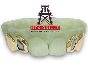 May include: Gold grillz with a green mold, featuring the text "HTX GRILLZ HOME OF THE GRILLZ".