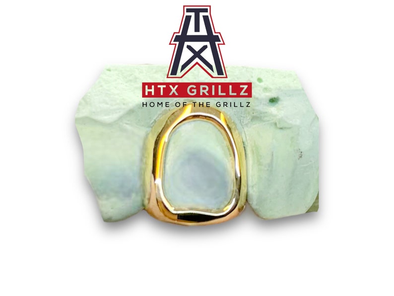 Op de afbeelding: Gouden grillz voor &eacute;&eacute;n tand, geplaatst in een mal. De grillz zijn gevormd als een afgerond rechthoek.