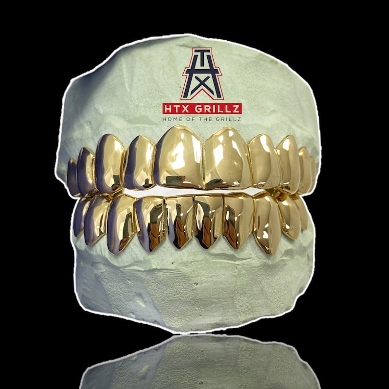 May include: Gold teeth grillz in a mold, with the text "HTX GRILLZ HOME OF THE GRILLZ" on the mold.