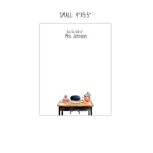 May include: A white notepad with the text "from the desk of Mrs. Johnson" at the top. The bottom of the notepad features a watercolor illustration of a desk with books, an apple, a plant, and a chair. The notepad measures 4" x 5.5".