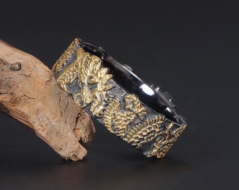 May include: A black and gold ring with a detailed floral design. The ring is made of metal and has a textured finish.