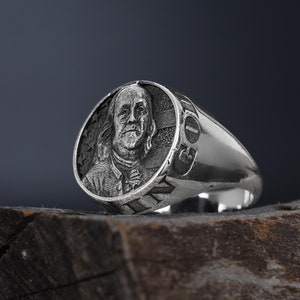 Könnte beinhalten: Ein silberner Ring mit einer runden Oberfläche, die eine detaillierte Gravur von Benjamin Franklin zeigt. Der Ring hat ein glattes Band und die Inschrift "1732" an der Seite.