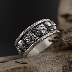 K&ouml;nnte beinhalten: Ein silberner Ring mit einer strukturierten Band, die abwechselnd Sch&auml;del und Rosen zeigt.