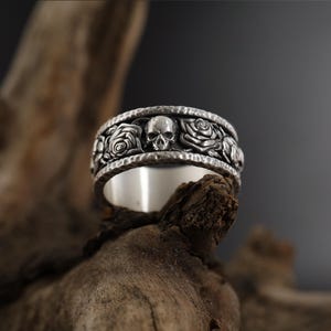 K&ouml;nnte beinhalten: Ein silberner Ring mit einem Totenkopf- und Rosenmotiv. Der Ring ist texturiert und hat eine geh&auml;mmerte Oberfl&auml;che.