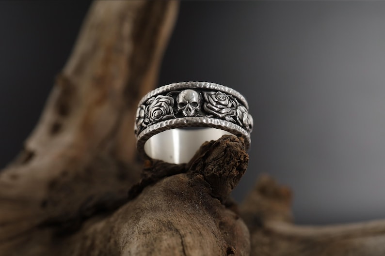 K&ouml;nnte beinhalten: Ein silberner Ring mit einem Totenkopf- und Rosenmotiv. Der Ring ist texturiert und hat eine geh&auml;mmerte Oberfl&auml;che.