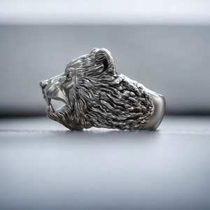 Roaring bear head ring, wild animal inspired statement jewelry, symbolic warrior band, and handcrafted bold accessory designed for those who are drawn to strength, dominance, and fearless energy. This striking ring features a detailed roaring bear head motif with open jaws, sharp teeth, and intense engraved textures, creating a powerful and aggressive appearance inspired by nature, Viking symbolism, and primal force.