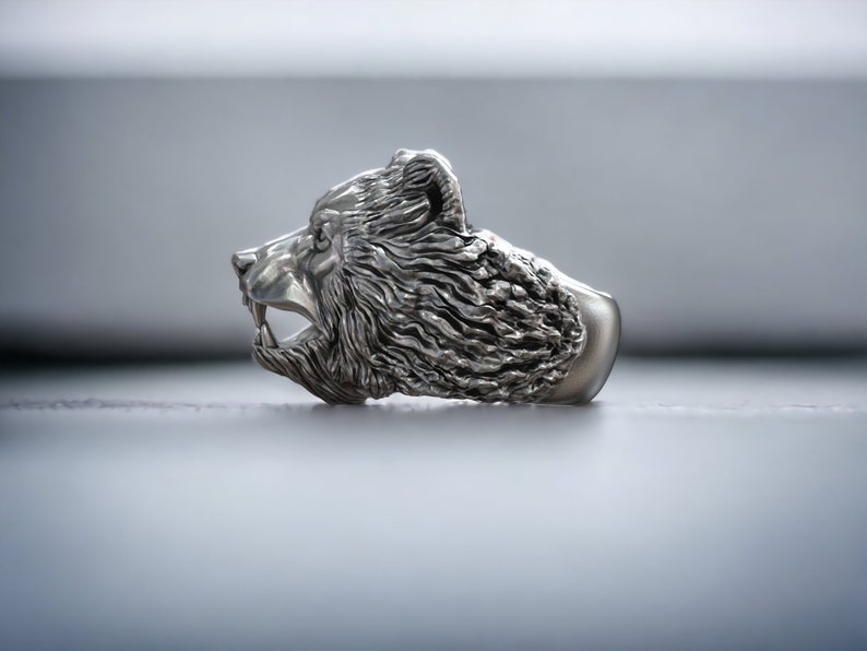 Roaring bear head ring, wild animal inspired statement jewelry, symbolic warrior band, and handcrafted bold accessory designed for those who are drawn to strength, dominance, and fearless energy. This striking ring features a detailed roaring bear head motif with open jaws, sharp teeth, and intense engraved textures, creating a powerful and aggressive appearance inspired by nature, Viking symbolism, and primal force.