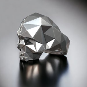 May include: A silver ring shaped like a geometric skull. The ring is made of many small triangles that create a faceted look.