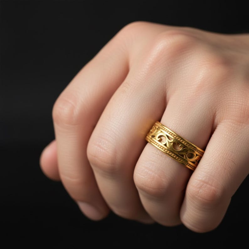 Puede incluir: Un anillo dorado con un intrincado dise&ntilde;o calado. El anillo, que se lleva en un dedo, presenta un patr&oacute;n repetitivo de formas arremolinadas. La superficie del anillo es pulida y reflectante. El fondo es oscuro.