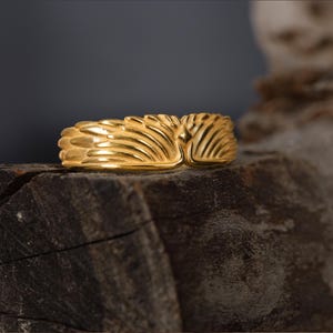 May include: A gold ring with a textured design resembling a pair of wings.